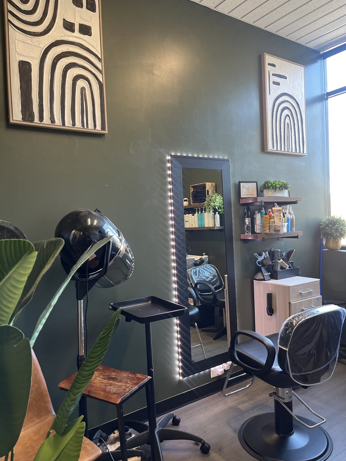 Stacy’s suite: dark green walls, a styling chair, lit mirror and hooded dryer